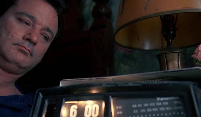A screenshot from the movie Groundhog Day with Bill Murray watching a clock.